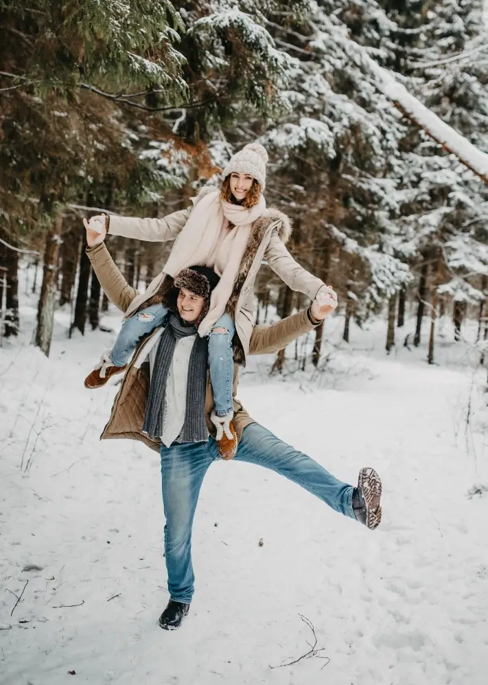 Happy young couple outside in a wintery forest. The man is holding the woman on his shoulders.