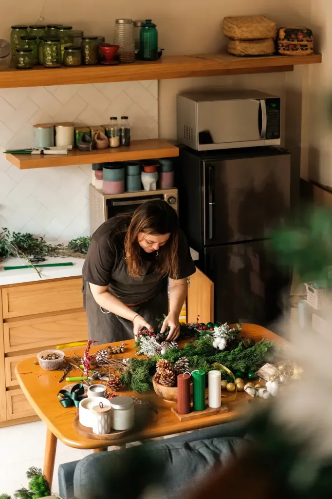 Woman in a kitchen making a fresh Christmas wreath.