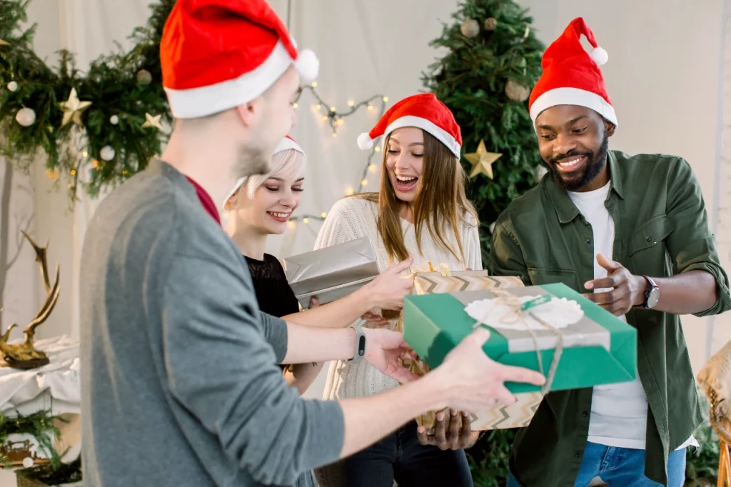 Excited coworkers exchanging presents in front of a Christmas tree.