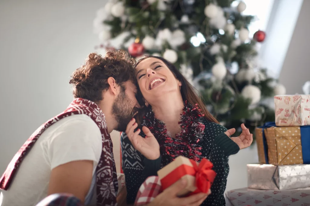 Happy couple laughing together with gifts in front of a Christmas tree.