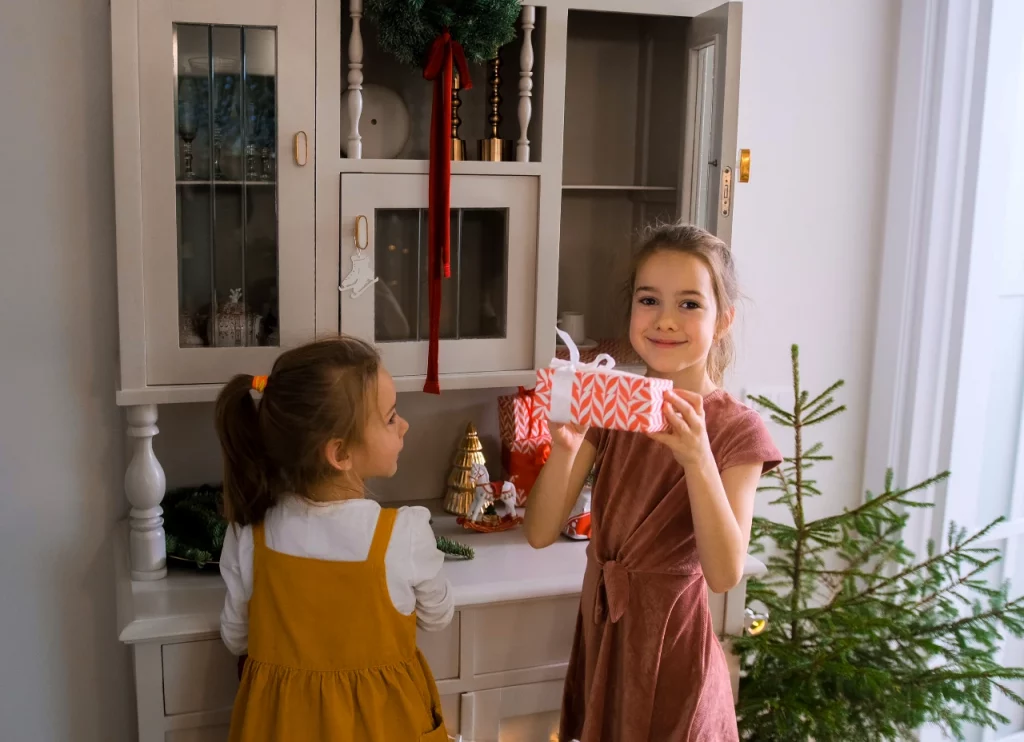 Two girls in front of a kitchen side table, holding Christmas presents